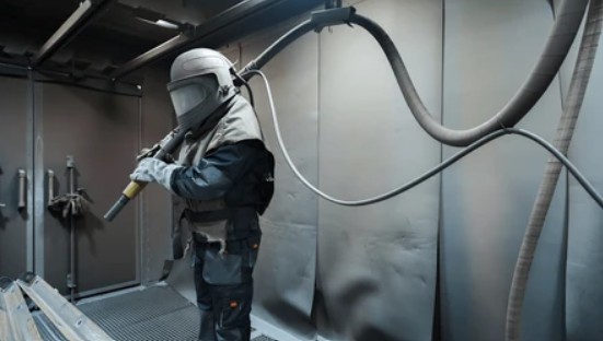 Operador realizando sand blast industrial en cabina